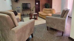 A living room with beige sofas, a television, a fan, and a door.