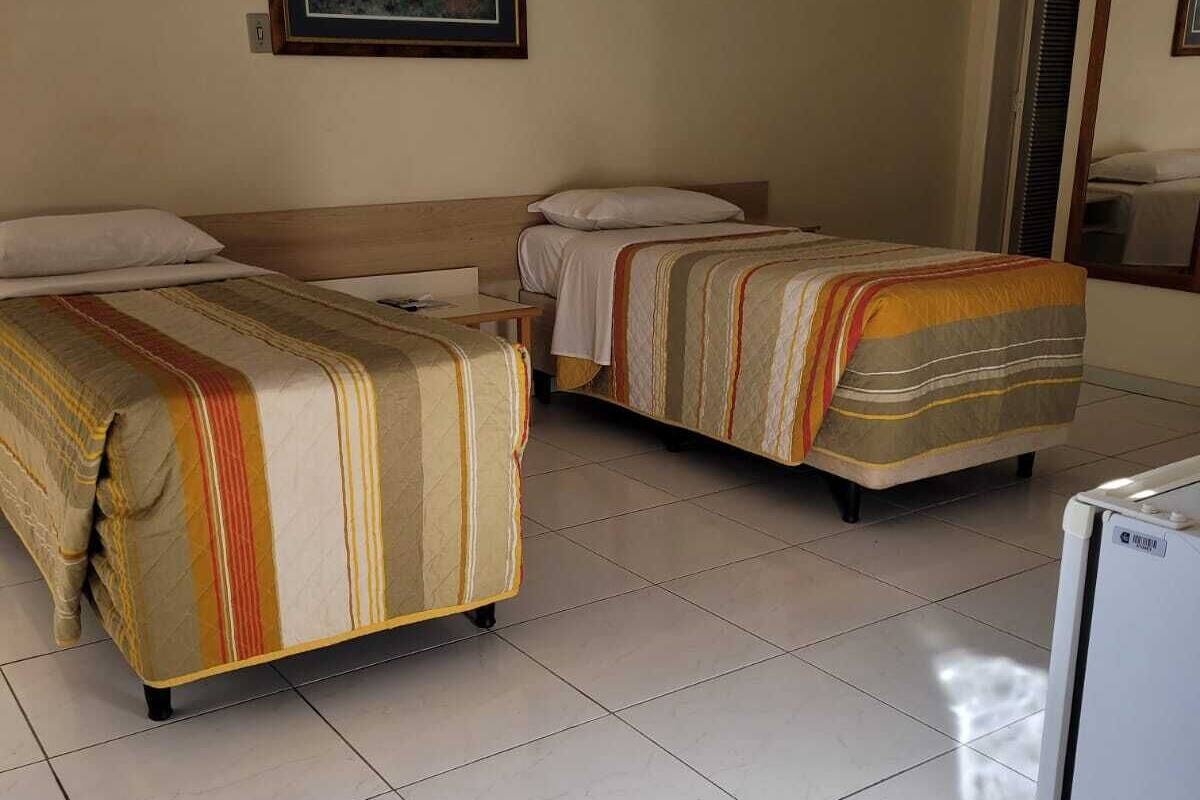A hotel room with two beds, a small table, a refrigerator, and a framed picture on the wall.