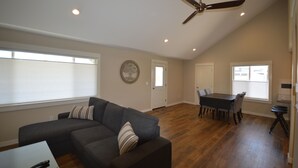 A spacious living room with a sectional sofa, a dining table with chairs, a ceiling fan, and a large window. - Boyne Bungalow (Boyne City)