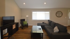 A living room with a flat-screen TV, a sofa, a coffee table, and a chair. - Boyne Bungalow (Boyne City)