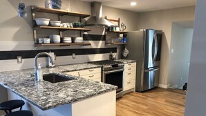 A modern kitchen with a granite countertop, stainless steel appliances, and a bar stool area. - Boyne Bungalow (Boyne City)