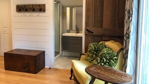 Une pièce comprenant une commode en bois, un canapé orné d’un coussin à volants, une petite table en bois et un miroir au-dessus d’un lavabo.
