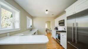 A modern kitchen with white cabinetry, a stainless steel refrigerator, and a wooden floor. - Riversbye: Historic luxury riverfront retreat (Boyne City)