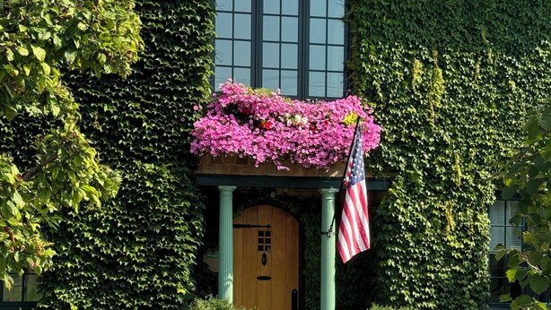 A building with a green ivy-covered facade, a wooden front door, and a flag. - Riversbye: Historic luxury riverfront retreat (Boyne City)
