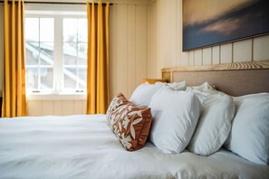 A hotel room with a bed, a window with curtains, and a painting on the wall.