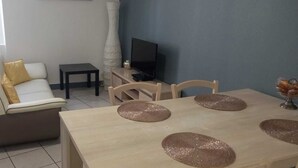 A living room with a sofa, a small table, a TV, and a dining table with placemats. - Joli Appartement Avec 2 Chambres (Périgueux)