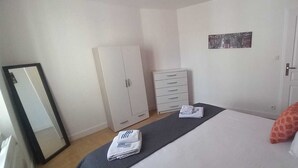 A bedroom with a bed, a wardrobe, a dresser, and a door. - Joli Appartement Avec 2 Chambres (Périgueux)