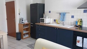A compact kitchen with a refrigerator, microwave, sink, and a small dining area with a table and chairs. - Joli Appartement Avec 2 Chambres (Périgueux)