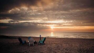 A beach with two chairs and a table facing the ocean at sunset.