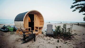 A wooden barrel-shaped structure on a beach with a chair and a bench inside.