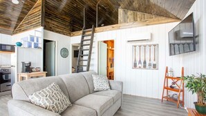 Una sala de estar con sofá, escalera, televisor y techo de madera.