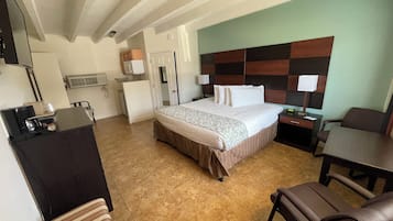 Habitación de hotel con cama, escritorio, silla, mesita y kitchenette.