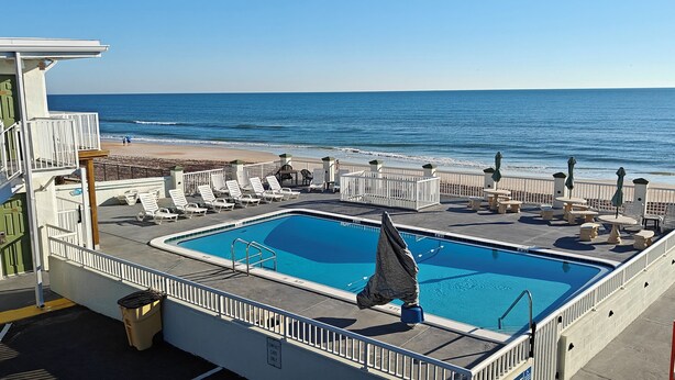 A pool area with lounge chairs and a view of the beach. - Oceanfront Inn and Suites (Ormond Beach)