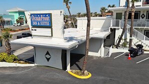 A building with a sign for OceanFront Inn & Suites, a parking area, and a motorcycle parked in front. - Oceanfront Inn and Suites (Ormond Beach)