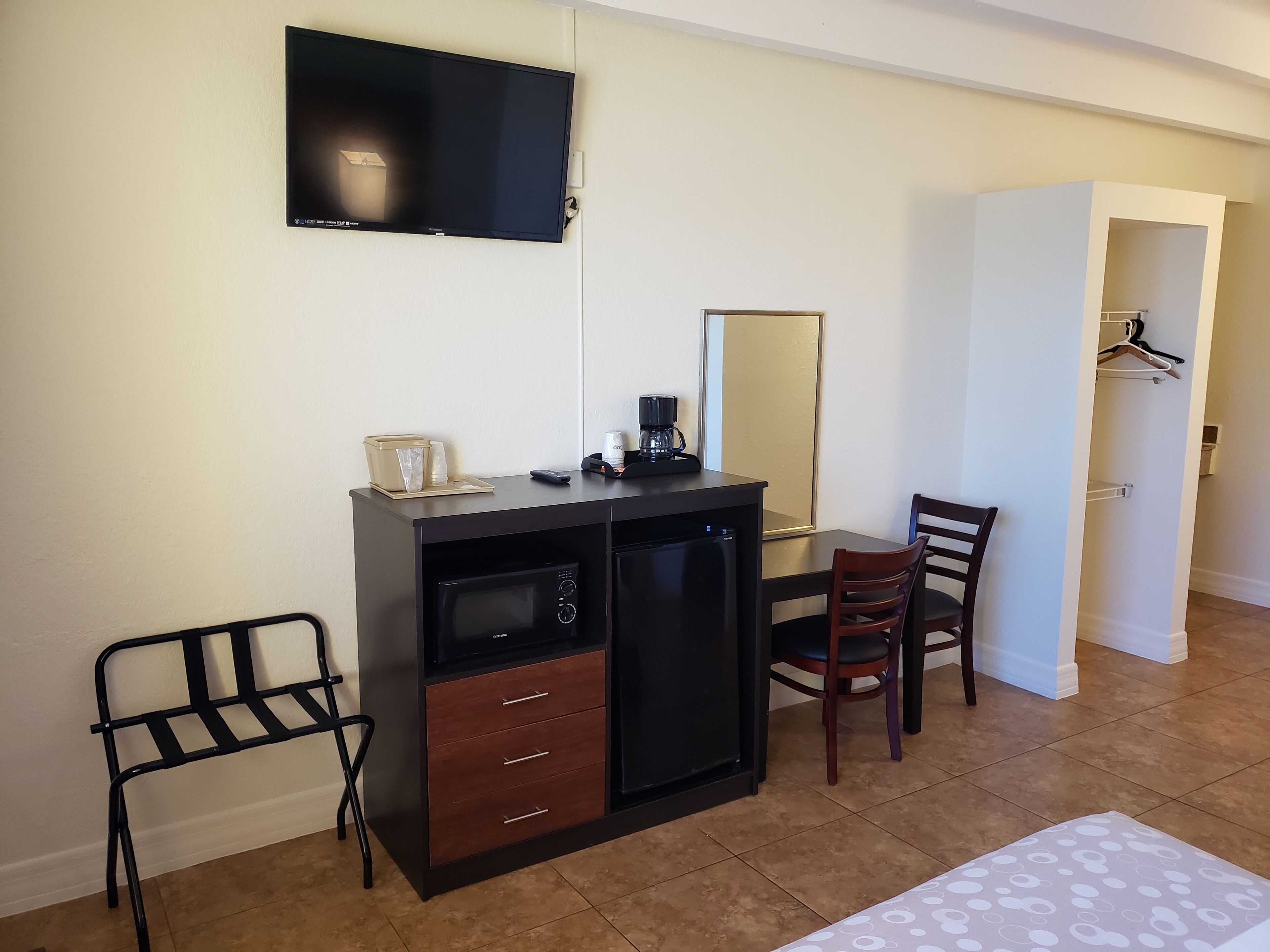 Una habitación compacta con kitchenette, televisor montado en la pared, una mesa de comedor con sillas y un vestidor.