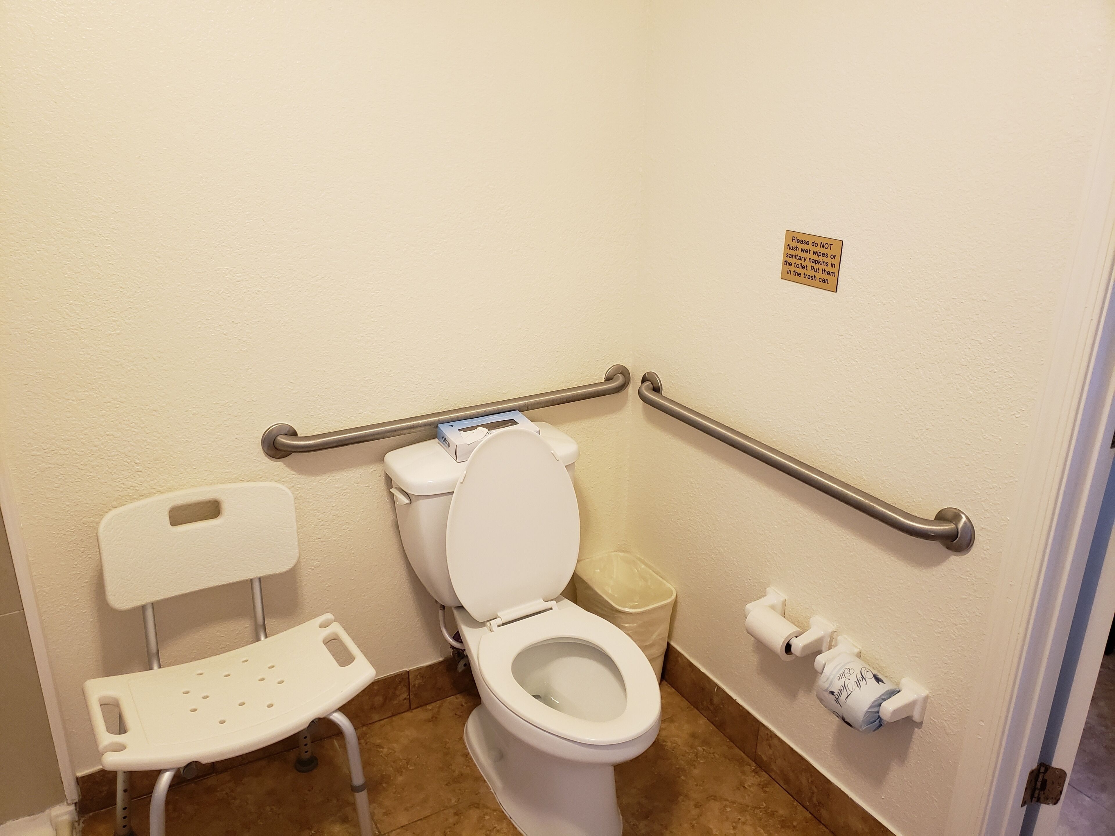 Une salle de bain avec des toilettes blanches, un banc blanc et une barre d’appui.
