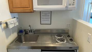 A compact kitchen with wooden cabinets, a microwave, a sink, and a built-in refrigerator.