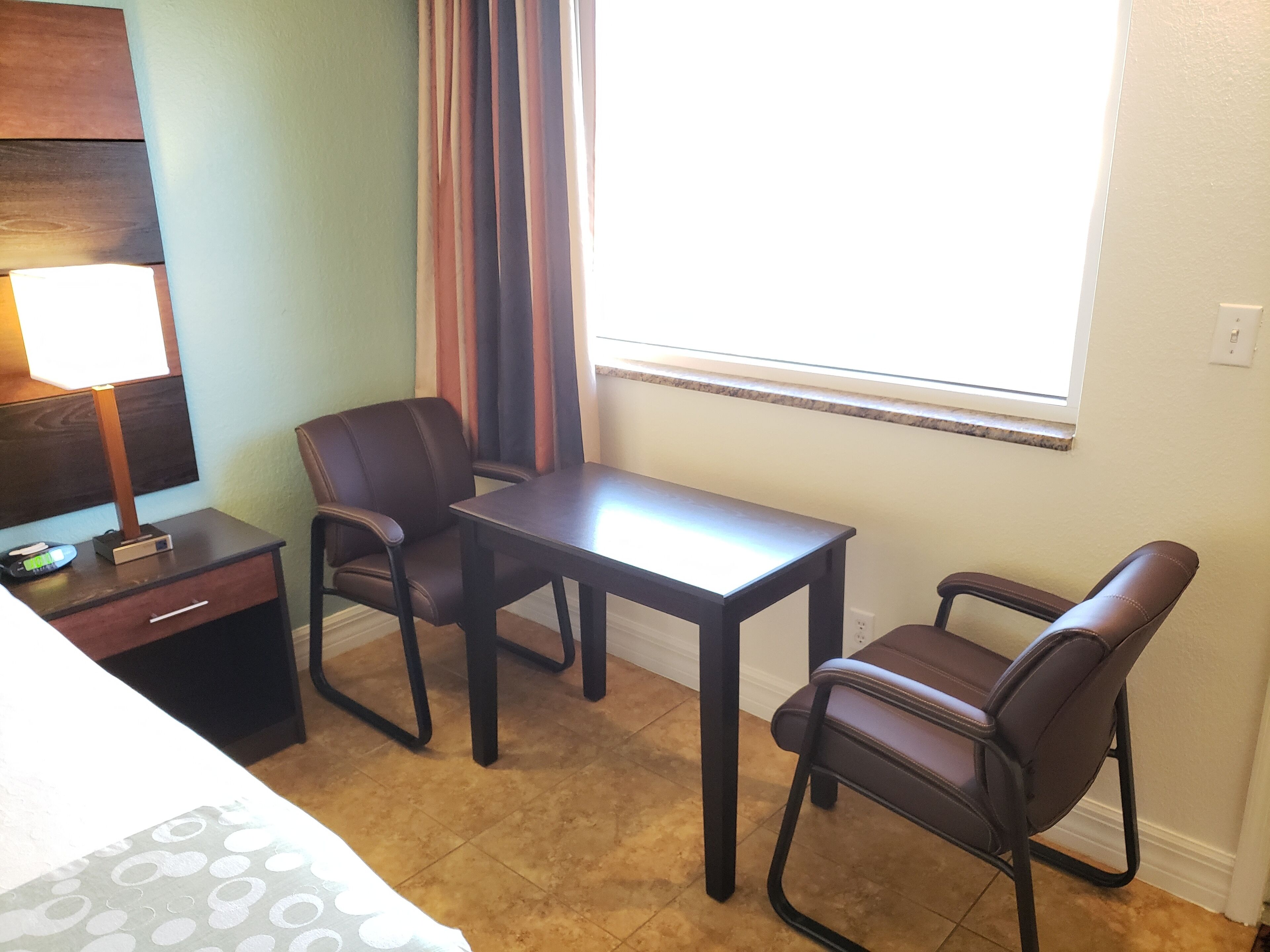 Une petite pièce comprenant un bureau, deux chaises, une lampe et une fenêtre avec des rideaux.