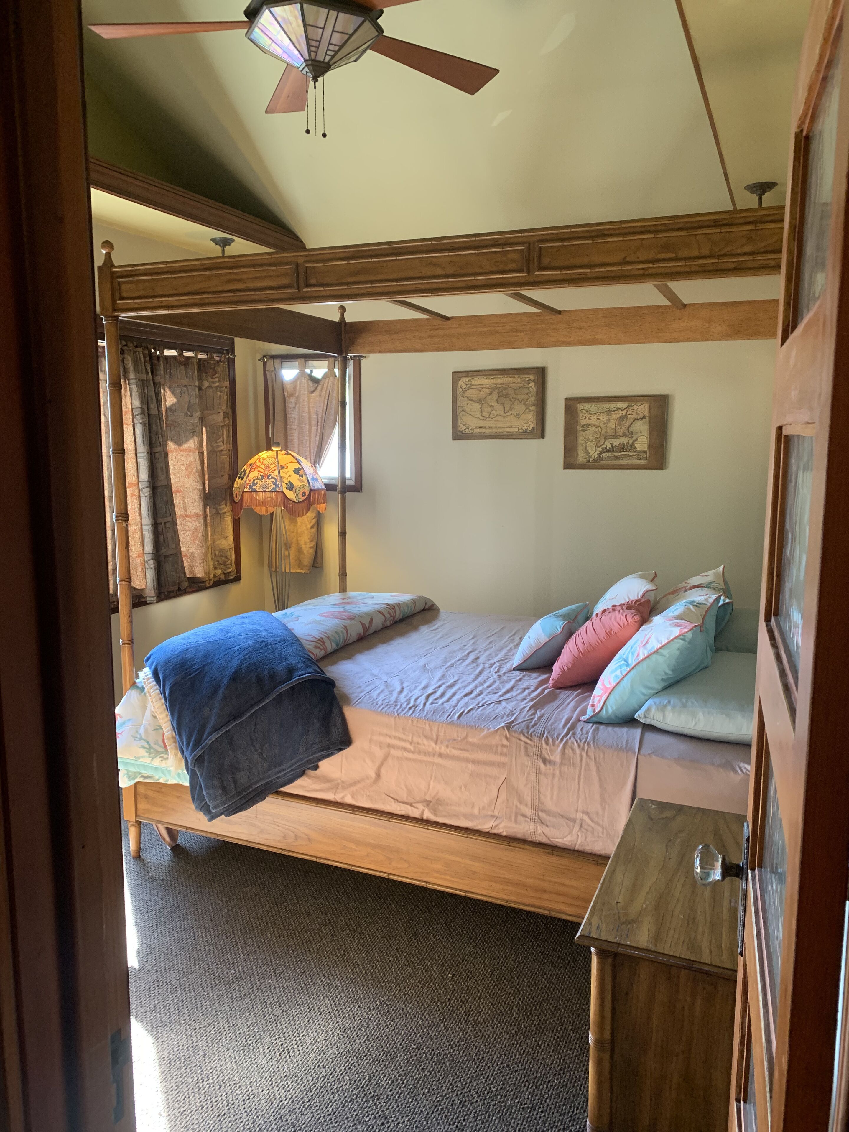 Una camera da letto con un letto, una testiera in legno, una ventola a soffitto, una mappa appesa al muro e una finestra con tende.