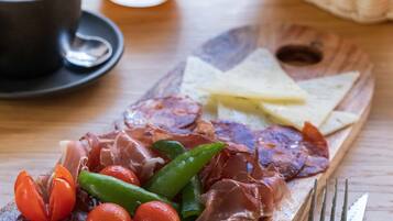 A charcuterie board with various meats, cheese, and vegetables, accompanied by a glass of orange juice and a basket of bread.
