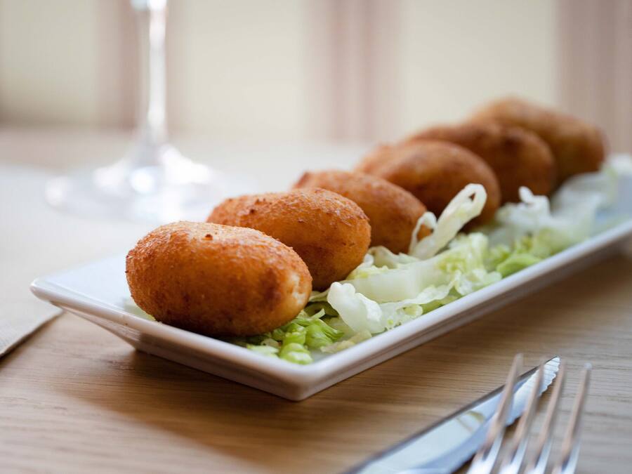 Un plato de croquetas acompañado de una copa de vino blanco sobre una mesa de madera.