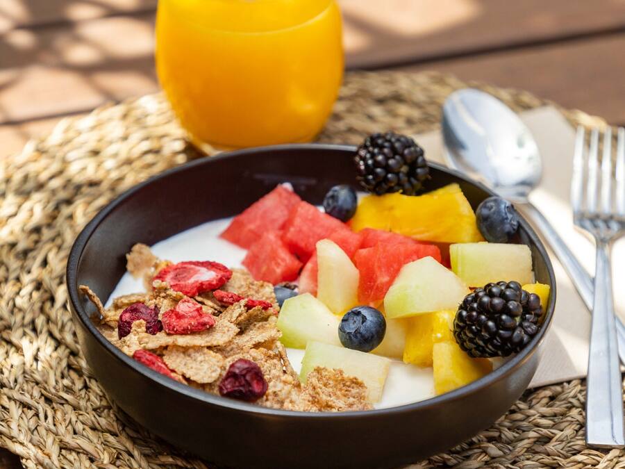 A bowl of cereal with fruits and a glass of orange juice on a woven placemat.
