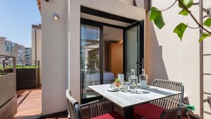 A modern outdoor dining area with a table and chairs, a glass door leading to a room, and a view of the cityscape in the background. - Joe's Gomila Boutique Hotel (Palma de Mallorca)