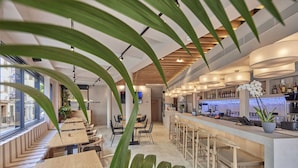 A modern bar area with wooden tables and chairs, a long counter with bar stools, and a bar stocked with bottles. - Joe's Gomila Boutique Hotel (Palma de Mallorca)