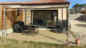 Eine überdachte Terrasse mit Tisch und Stühlen, einem Grill und Blick ins Innere durch Glastüren.