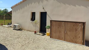 Ein Gebäude mit beige-farbener Fassade, einer Holztür, einem kleinen Fenster und einer Schotterauffahrt.