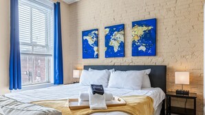 Ett hotellrum med en säng, ett träbricka med handdukar, en världskarta på väggen och ett fönster med gardiner.