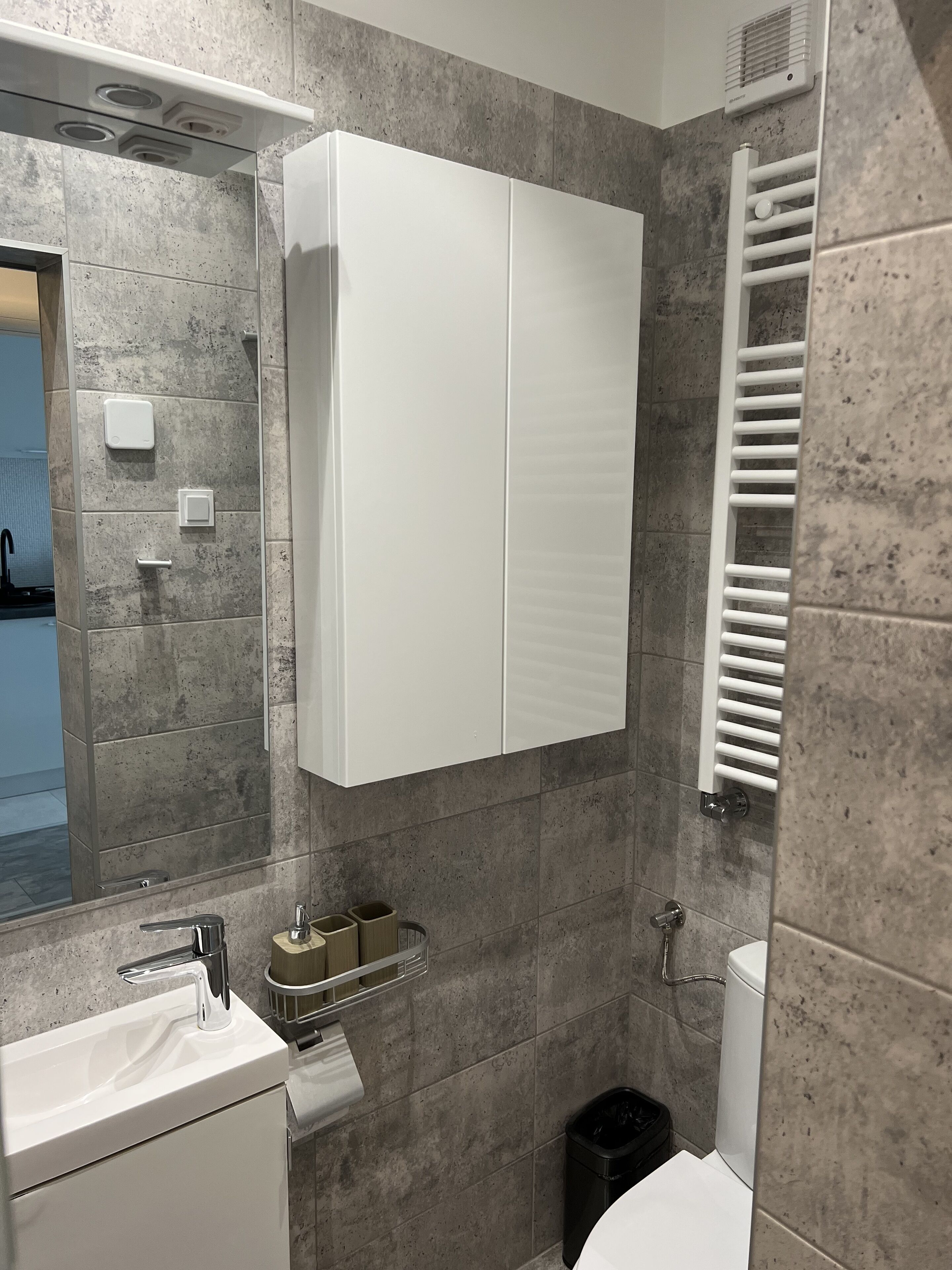A modern bathroom with a white cabinet, a sink, a mirror, and a towel rack.