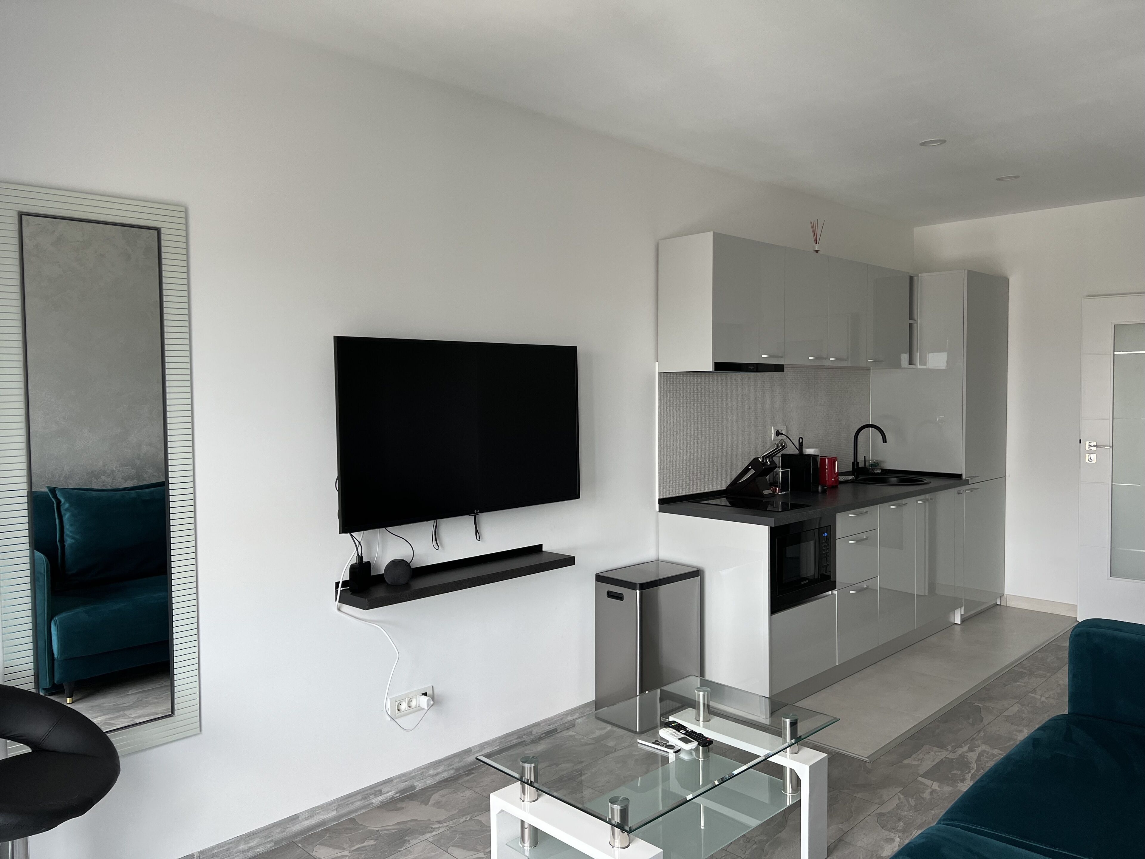 A modern living room with a flat-screen TV, a glass coffee table, and a teal sofa.