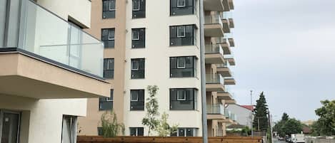 A multi-story residential building with balconies, a street view, and a wooden fence.