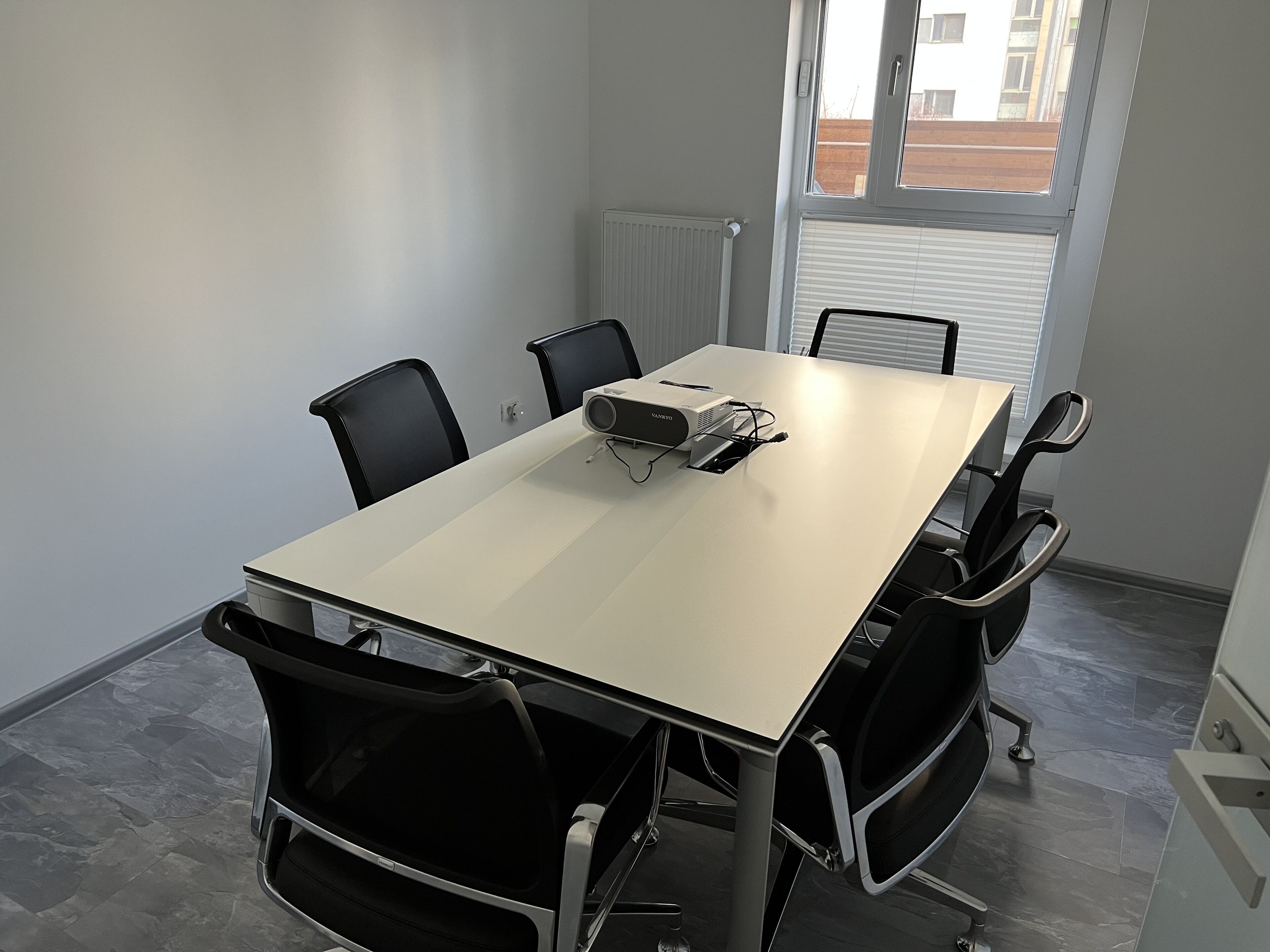 A conference room with a white table, black chairs, a projector, and a window with blinds.