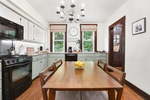 A kitchen with white cabinets, a wooden dining table, and a chandelier.
