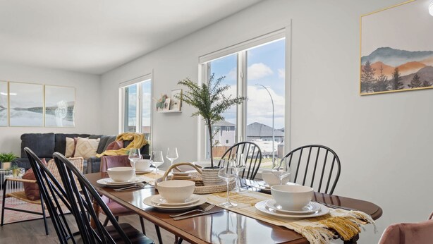 A dining area with a long table set for six, surrounded by chairs, with a view of the outdoors through large windows.