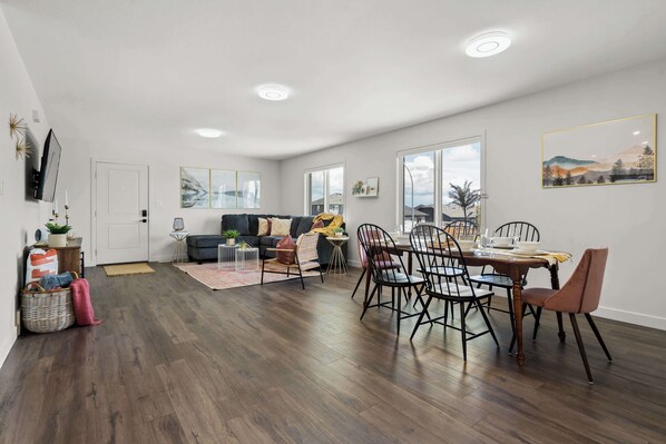 A spacious living room with a dining area, hardwood floors, and large windows.