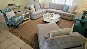 A living room with a sectional sofa, a patterned armchair, a glass coffee table, and a small side table.
