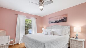 A bedroom with a large bed, a nightstand with a lamp, a chair, and a ceiling fan.
