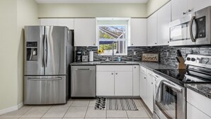 A modern kitchen with stainless steel appliances, white cabinets, and a view of the outdoors through a window.