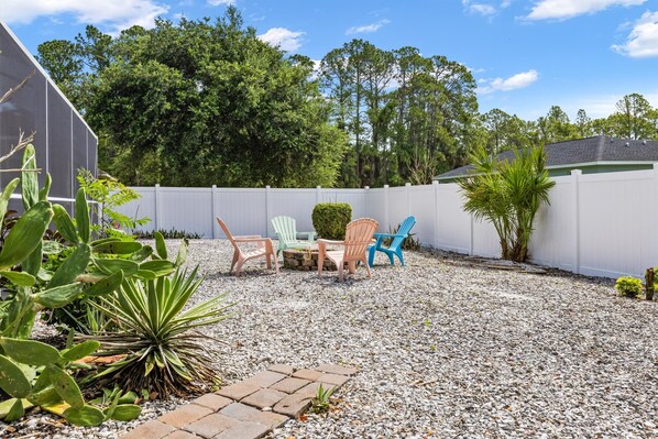 A patio area with a seating arrangement, a white fence, and surrounding greenery. - Casa Azul! 11min - warm mineral springs, 25min - beaches! HEATED Pool & floats! (North Port)