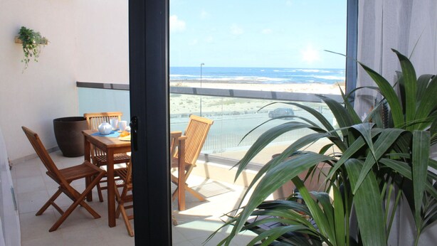 Een balkon met uitzicht op het strand, houten meubilair en planten in potten.