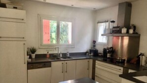 A kitchen with white cabinets, a black countertop, a window, and a stainless steel range hood. - Maison Dans Domaine Avec Piscine (Le Tholonet)