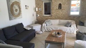A living room with a dark sofa, a light-colored sofa, a wooden coffee table, and a stone wall. - Maison Dans Domaine Avec Piscine (Le Tholonet)