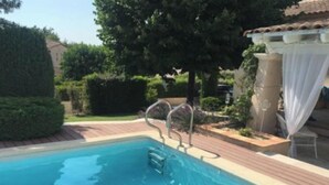A swimming pool with a metal ladder, surrounded by a wooden deck and greenery. - Maison Dans Domaine Avec Piscine (Le Tholonet)