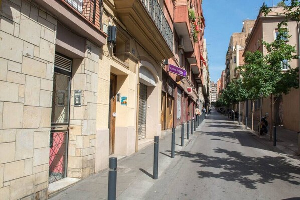 A narrow urban street lined with multi-story buildings, featuring balconies and storefronts.