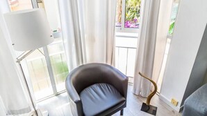 A modern room with a black leather chair, a white floor lamp, and a view of a balcony with plants and a railing.