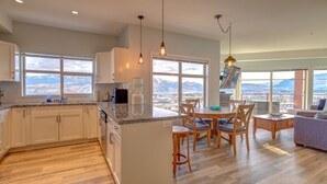 Une cuisine moderne dotée d’un grand îlot central, d’une table à manger en bois et de chaises, offrant une vue panoramique sur les montagnes.