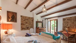 A bedroom with a bed, a nightstand with a lamp, a dresser, a mirror, and a window with a view of greenery. - Villa Olmo With Private Pool (Castel di Lucio)
